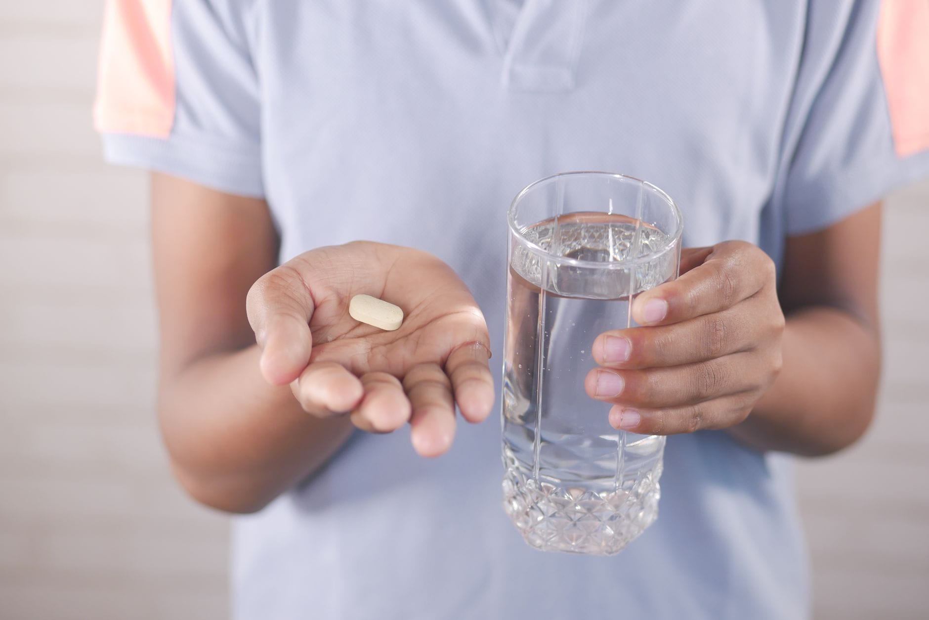 An adult taking a B12 tablet with a glass of water